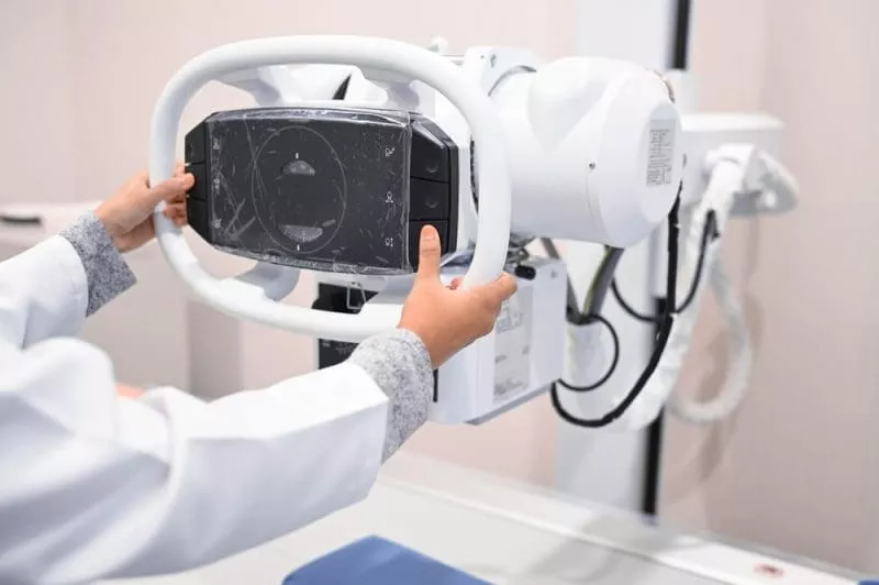 Clinician adjusting a medical imaging device in a clinical examination room.