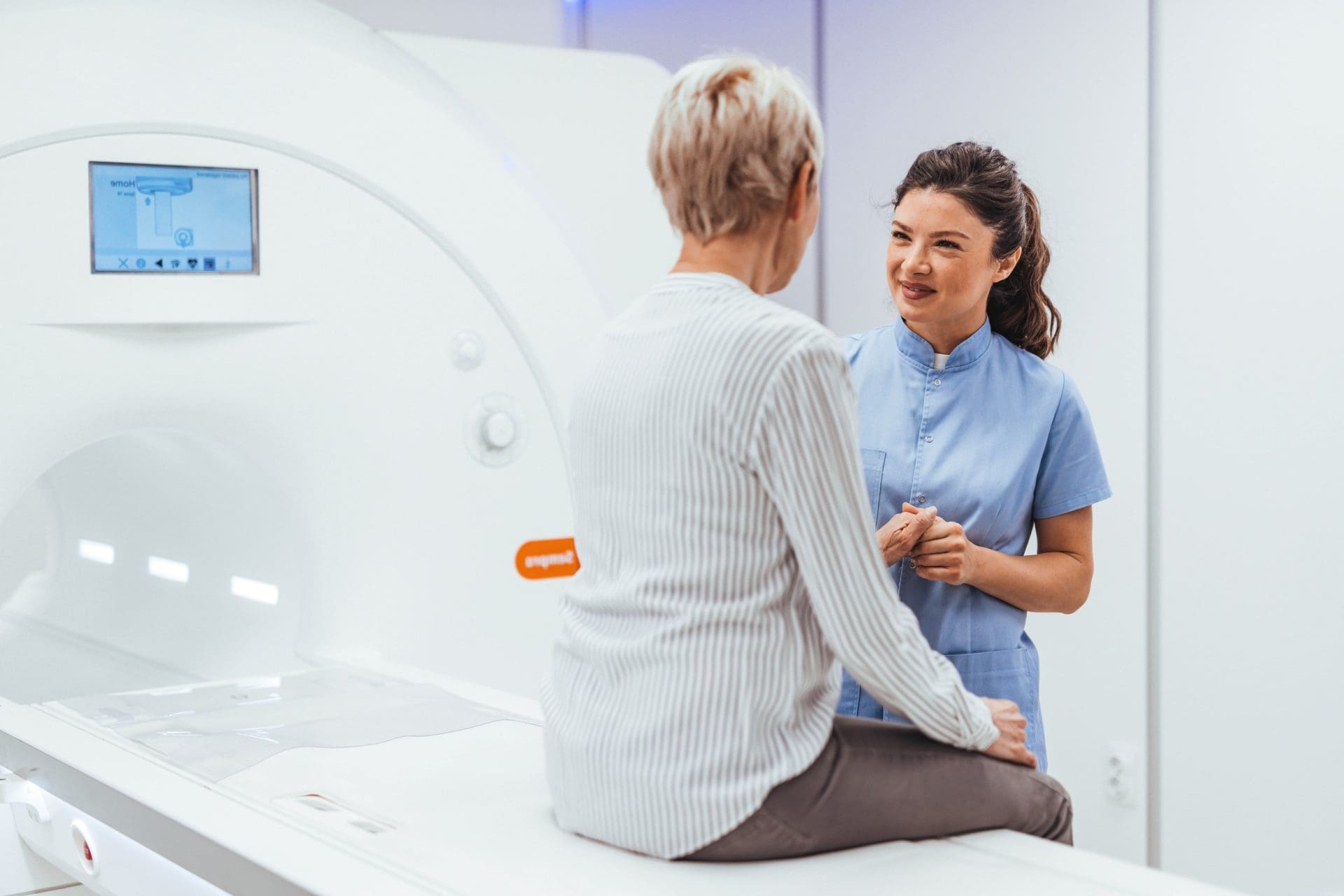 Healthcare professional speaking with a patient seated beside an MRI scanner.