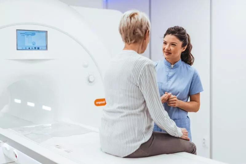 Healthcare professional speaking with a patient seated beside an MRI scanner.