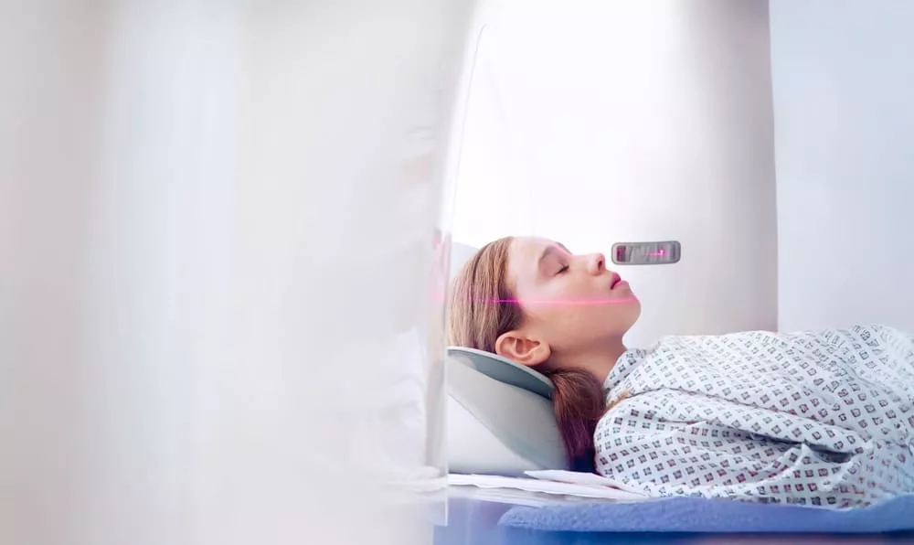Patient lying still in a CT scanner, with a positioning laser aligned across her face.