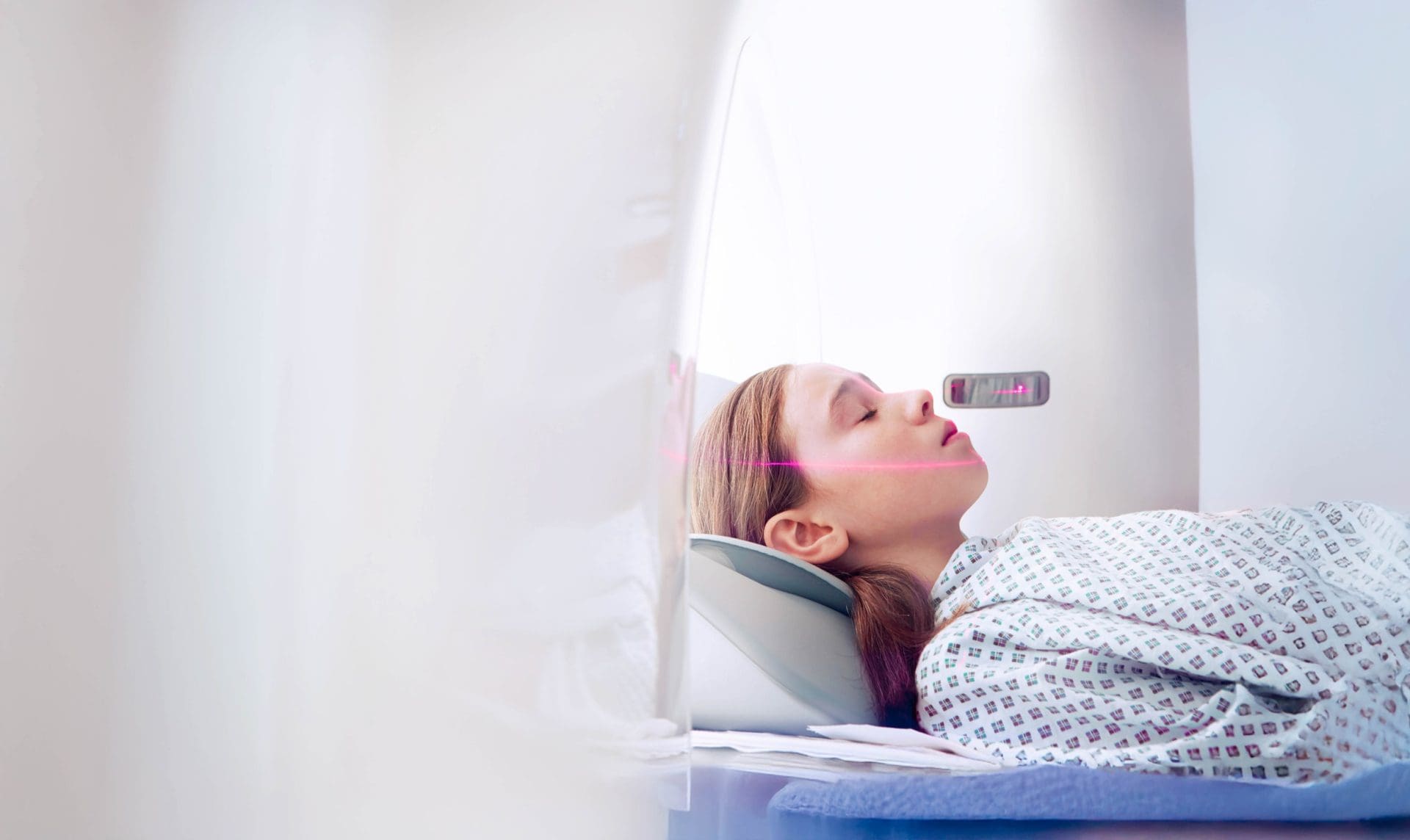 Patient lying still in a CT scanner, with a positioning laser aligned across her face.