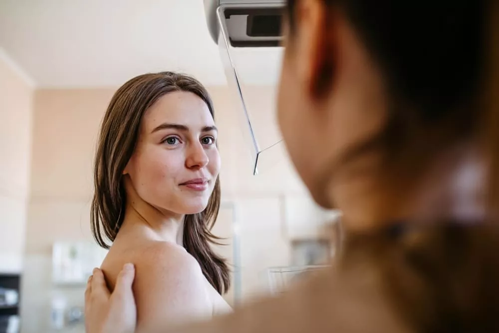 Woman undergoing a breast imaging exam, standing still while a clinician positions the scanner.