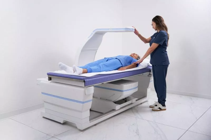 Clinician positioning an overhead imaging arm above a patient lying on a medical examination table.