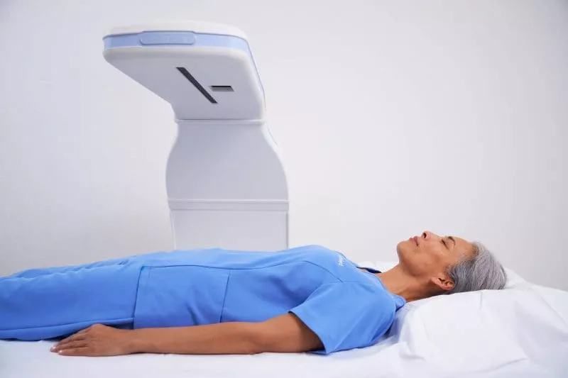 Patient lying on an imaging table beneath an overhead medical scanning device.