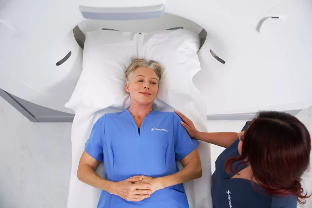 Patient lying calmly on an MRI scanner bed while a clinician offers reassurance beside them.