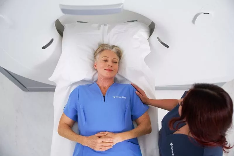 Patient lying calmly on an MRI scanner bed while a clinician offers reassurance beside them.
