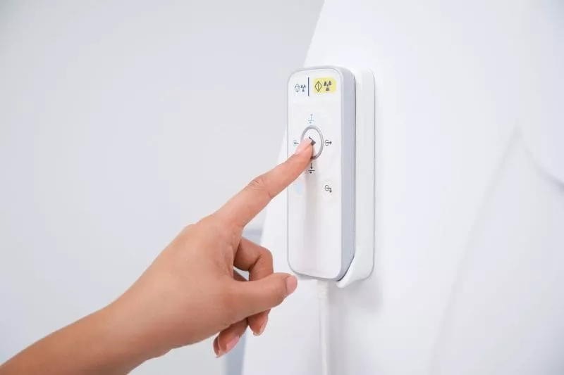 Hand pressing a control button on an MRI scanner wall panel.