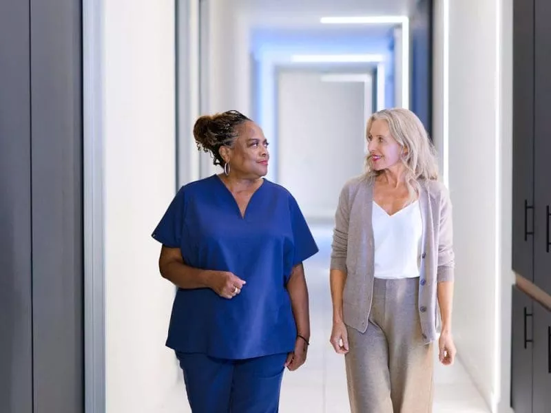 A clinician and a woman walk side by side down a bright, modern clinic corridor, talking.