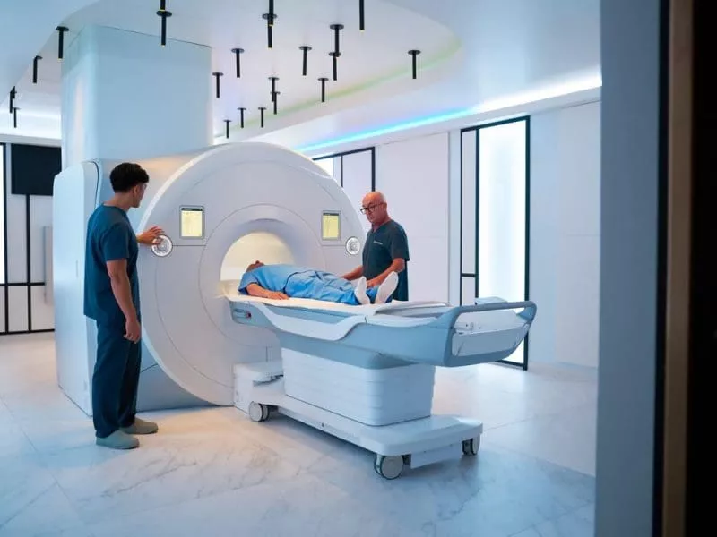 Patient on a table being positioned into an MRI scanner by two clinicians in a modern imaging room.