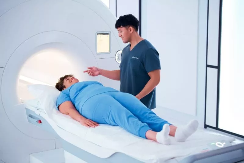 Clinician speaking reassuringly to a patient lying on a table as they are positioned into an MRI scanner.