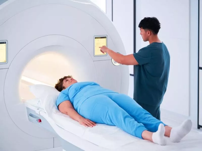 Patient lying on an MRI scanner bed while a clinician adjusts settings on the machine’s touchscreen.