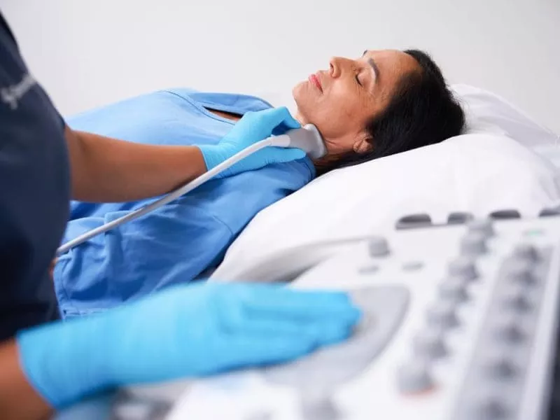 Clinician performing an ultrasound scan on a woman’s neck as she lies on an examination bed.